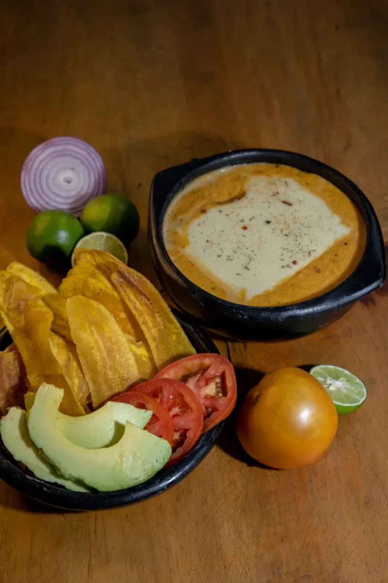 Cazuela de mariscos gratinada con patacones, aguacate y tomate sobre mesa de madera